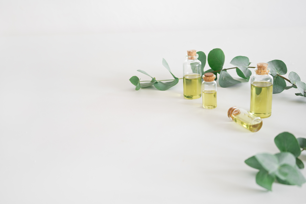 Small Bottles of Extra Oil on a Light Grey Surface surrounded by Leaves