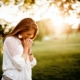 Woman with clasped hands standing outside under a tree praying and being thoughtful