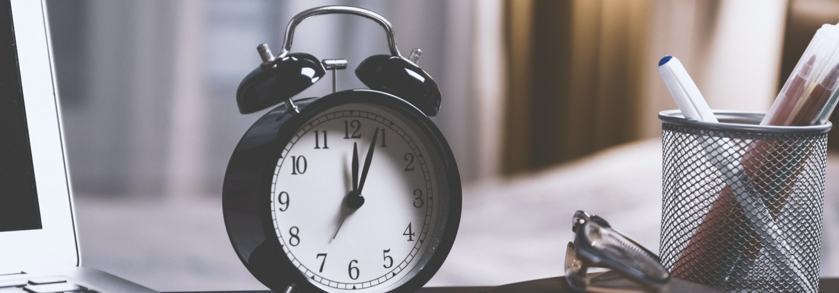 A black and white colour scheme. A black alarm clock with 12:05 on the clockface.