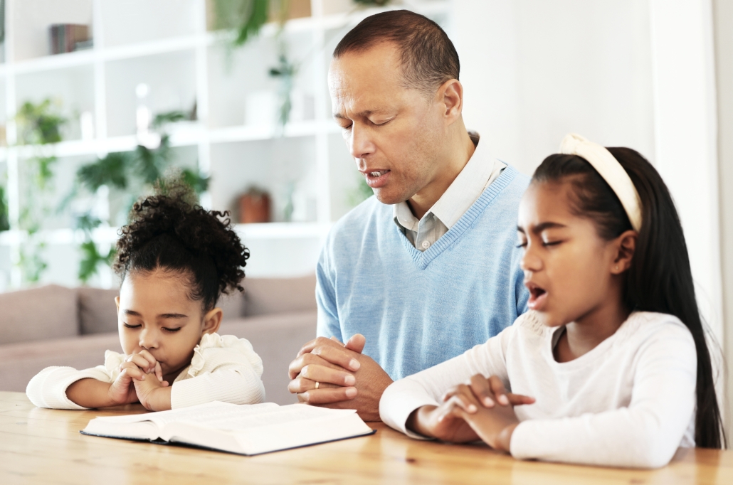 Family, worship and bible with father and kids praying at table for peace, religion and faith in their home. God, pray and children with parent for prayer, bible study or Jesus Christ praise together. Train up a child