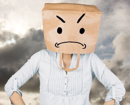 Woman feeling like a fraud where parents feel like imposters with hands on hip and covering head with brown paper bag against blue sky with white clouds