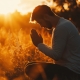 A man with a loyal heart towards God sits cross-legged in a serene field, hands clasped in prayer, soaking in the warmth of the setting sun amidst tall grass.