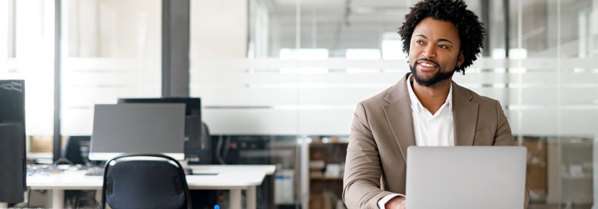 African-American young businessman working on his laptop in a contemporary office space with glass partitions on the backdrop. Concept of business and technology, bunner, panoramic view