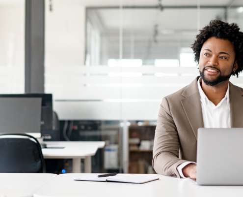 African-American young businessman working on his laptop in a contemporary office space with glass partitions on the backdrop. Concept of business and technology, bunner, panoramic view