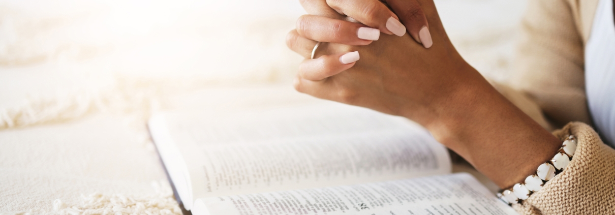 Prayer, bible and hands praying for religion, hope or help, spiritual or faith in home. God, christian and female or woman worship Jesus Christ or Holy Spirit with catholic text or book for peace
